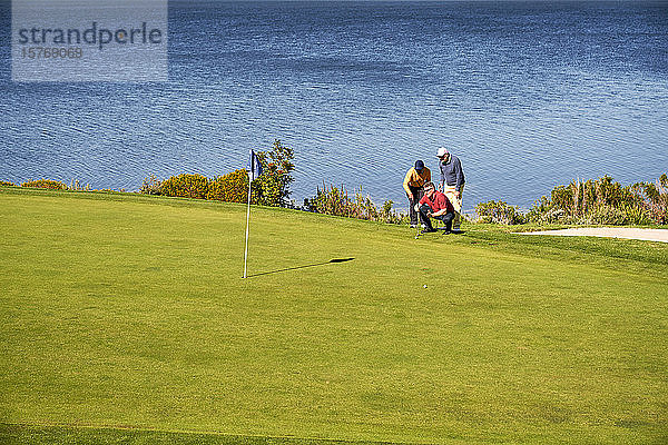 Männliche Golfer planen den Putt auf einem sonnigen Golfplatz am See