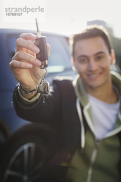 Porträt eines glücklichen jungen Mannes  der neue Autoschlüssel mit einem Schlüsselanhänger in Herzform hält