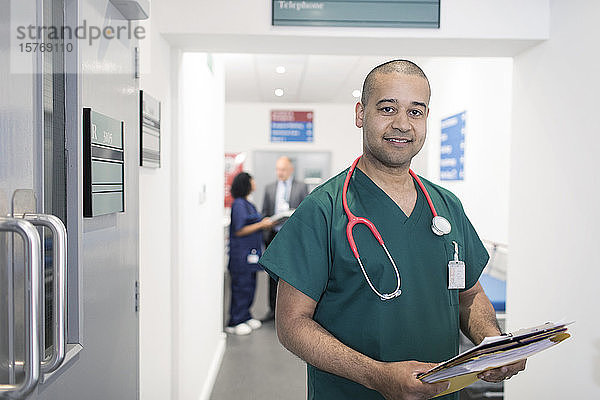 Porträt selbstbewusster männlicher Arzt mit Krankenblatt bei der Visite im Krankenhauskorridor