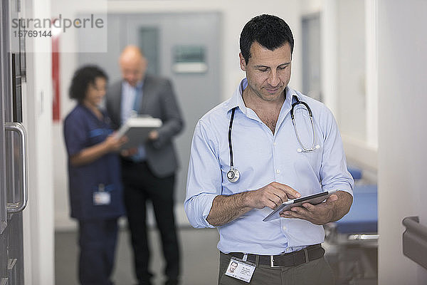 Männlicher Arzt mit digitalem Tablet im Krankenhausflur
