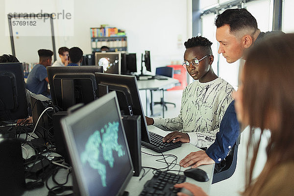 Männlicher Mittelschullehrer hilft einem Schüler bei der Benutzung eines Computers im Computerraum