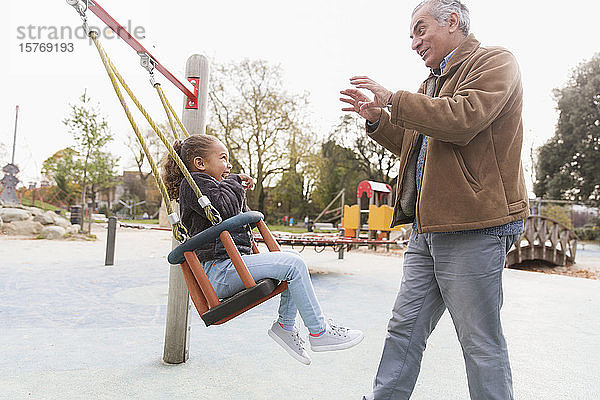 Großvater schiebt Enkelin auf Spielplatzschaukel