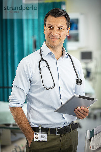 Porträt eines selbstbewussten männlichen Arztes  der ein digitales Tablet im Krankenhaus benutzt