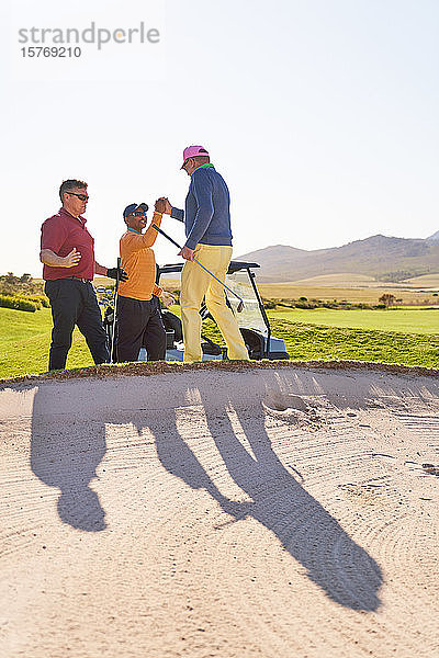 Männliche Golfer beim Feiern hinter dem sonnigen Golfbunker
