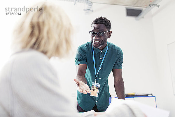 Männlicher Dozent einer Volkshochschule im Gespräch mit einem Studenten im Klassenzimmer