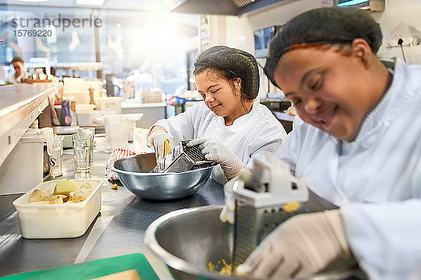 Lächelnde junge Frau mit Down-Syndrom reibt Käse in der Küche eines Cafés