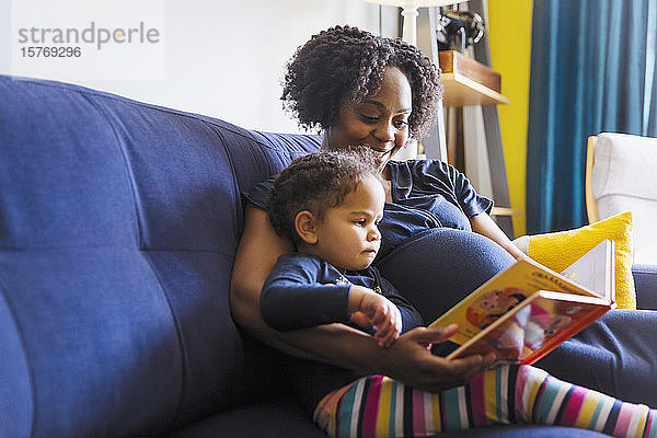 Schwangere Mutter und Tochter lesen ein Buch auf dem Sofa