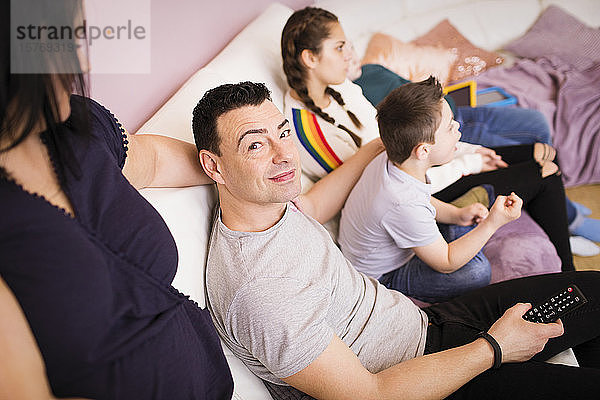 Porträt eines glücklichen Mannes  der mit seiner Familie auf dem Sofa fernsieht
