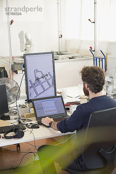 Männlicher Ingenieur  der Roboter programmiert  arbeitet am Laptop im Büro