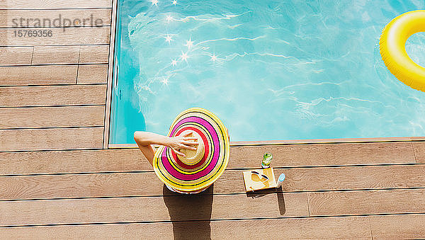 Frau mit Sonnenhut entspannt sich am sonnigen Pool