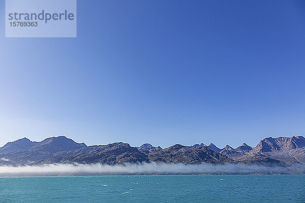 Blauer Himmel über majestätischer Berglandschaft und Meer Grönland