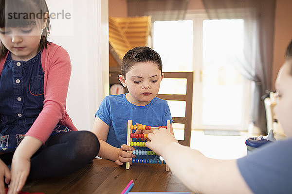 Junge mit Down-Syndrom und Geschwister spielen mit Spielzeug am Tisch