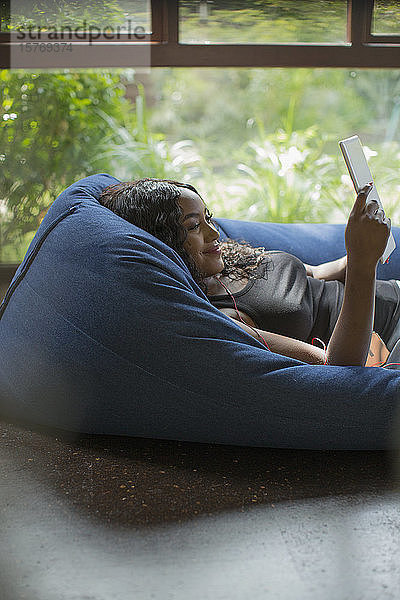 Glückliche junge Frau entspannt sich mit digitalem Tablet in Sitzsackstuhl
