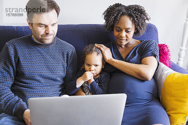 Schwangere Familie mit Laptop auf dem Sofa