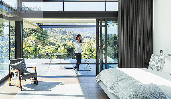 Frau  die in der Terrassentür eines modernen  luxuriösen Schlafzimmers mit einem Smartphone telefoniert
