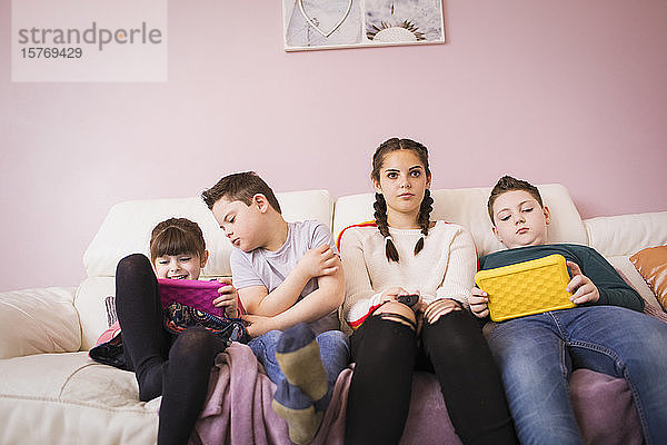 Mädchen und Bruder mit Down-Syndrom benutzen digitales Tablet auf dem Sofa