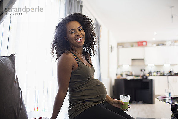 Portrait glückliche junge schwangere Frau trinkt grünen Smoothie