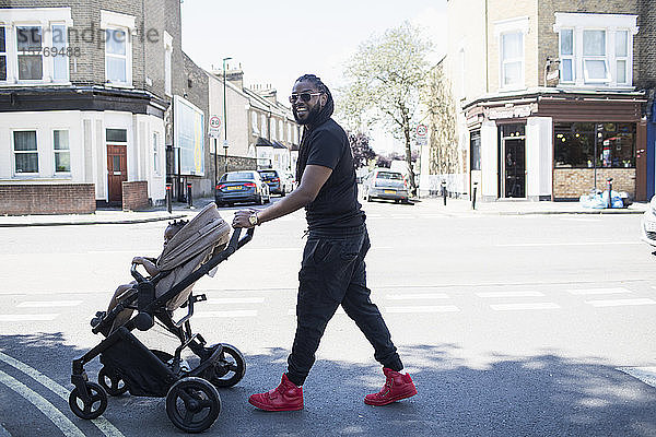 Porträt glücklicher Vater  der sein Kleinkind im Kinderwagen auf einer sonnigen Straße schiebt