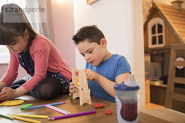 Konzentrierter Junge mit Down-Syndrom spielt mit Spielzeug am Tisch