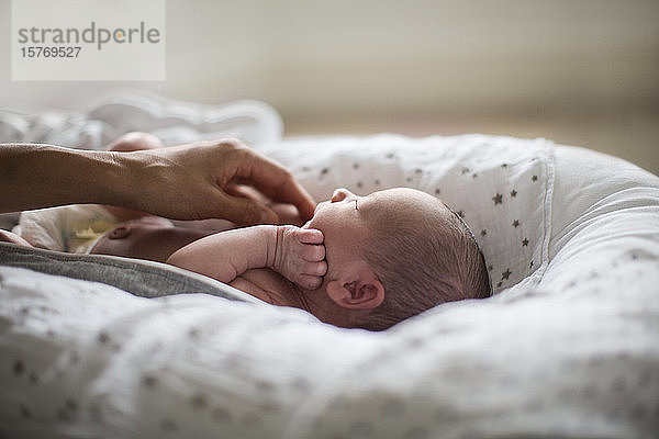 Mutter berührt niedlichen neugeborenen Baby-Sohn im Stubenwagen