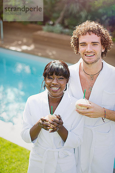 Portrait glückliches junges Paar in Bademänteln  das aus Kokosnüssen trinkt