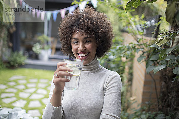 Porträt einer glücklichen jungen Frau  die auf einer Terrasse Wasser trinkt