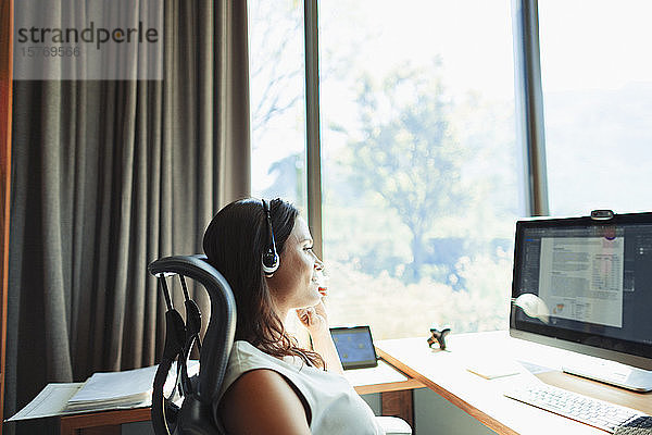 Geschäftsfrau mit Headset bei der Arbeit am Computer im sonnigen Heimbüro