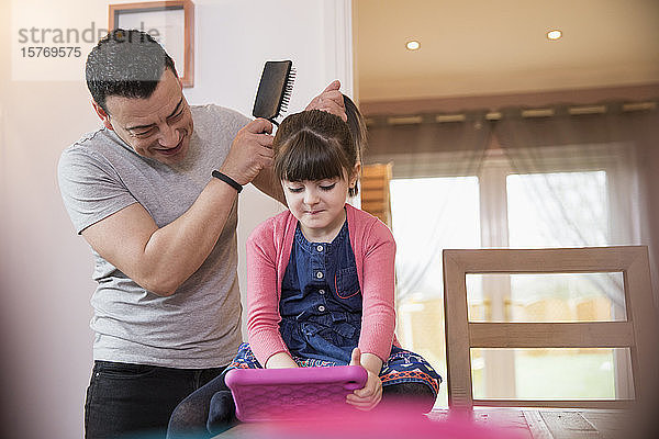Vater bürstet die Haare seiner Tochter mit einem digitalen Tablet