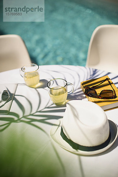 Tee und Sonnenhut auf dem sonnigen Terrassentisch im Sommer am Pool