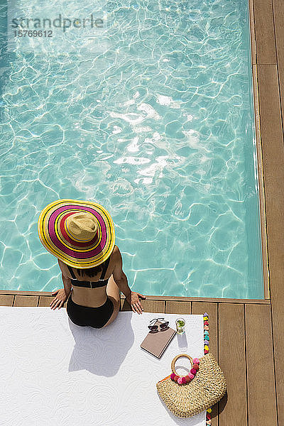 Frau in Sonnenhut und Bikini entspannt am sonnigen Pool