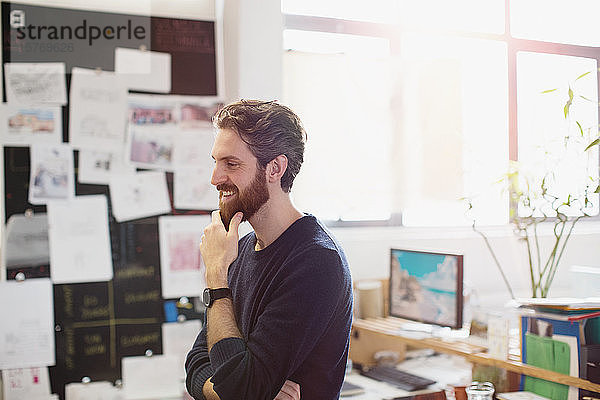 Glücklicher kreativer Geschäftsmann reibt sich im Büro den Bart