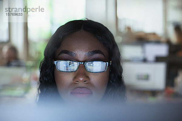 Konzentrierte junge Geschäftsfrau mit Brille arbeitet am Computer
