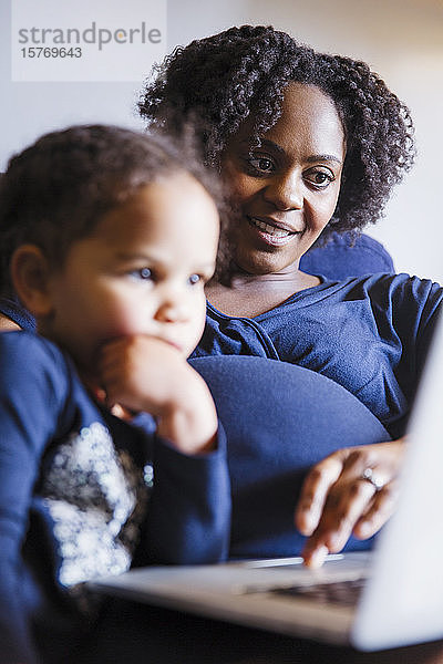 Schwangere Mutter und Tochter mit Laptop