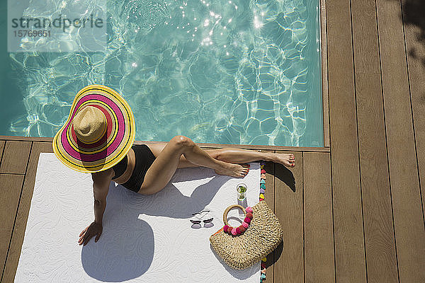 Frau mit Sonnenhut beim Sonnenbaden und Entspannen am sonnigen Sommerpool