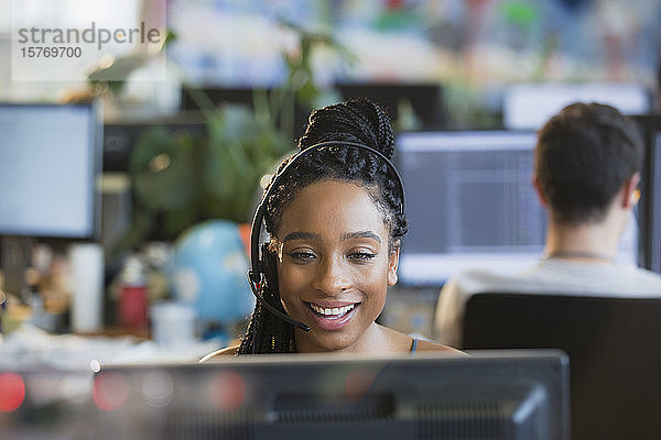 Lächelnde Geschäftsfrau mit Headset bei der Arbeit am Computer im Büro