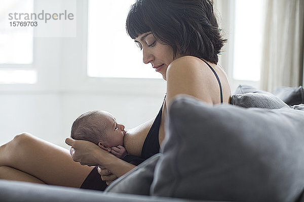 Mutter  die ihr neugeborenes Baby auf dem Sofa stillt