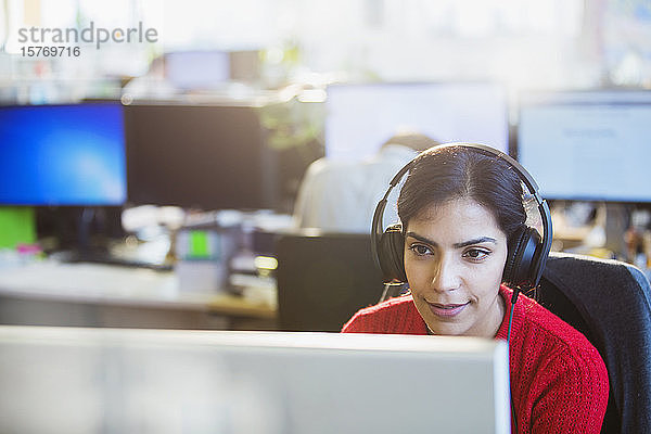 Geschäftsfrau mit Kopfhörern bei der Arbeit am Computer im Büro