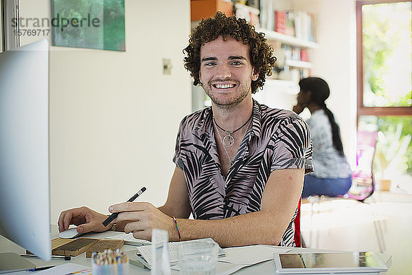 Porträt eines lächelnden jungen Mannes bei der Arbeit am Computer im Heimbüro
