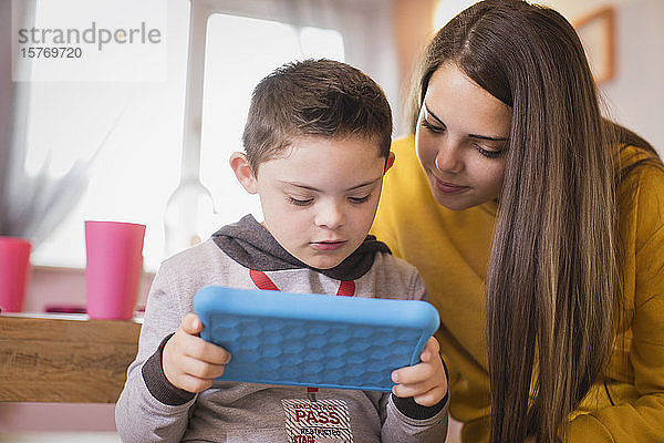 Mädchen beobachtet Bruder mit Down-Syndrom bei der Nutzung eines digitalen Tablets