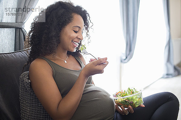 Glückliche junge schwangere Frau isst Salat