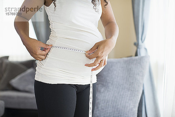 Schwangere Frau misst Bauch mit Maßband