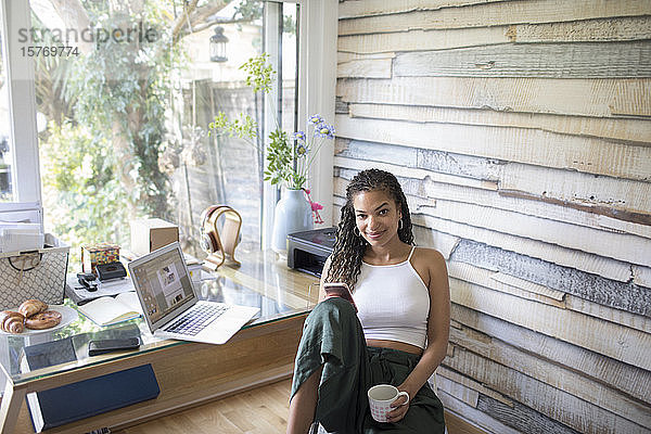 Porträt einer selbstbewussten jungen Frau  die im Büro zu Hause ein Smartphone benutzt