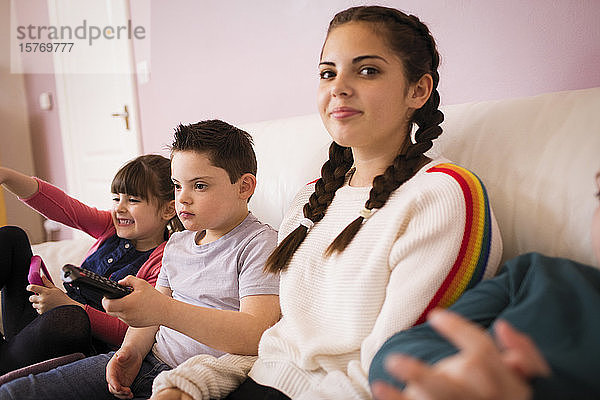 Porträt eines lächelnden Mädchens  das mit Geschwistern auf dem Sofa fernsieht