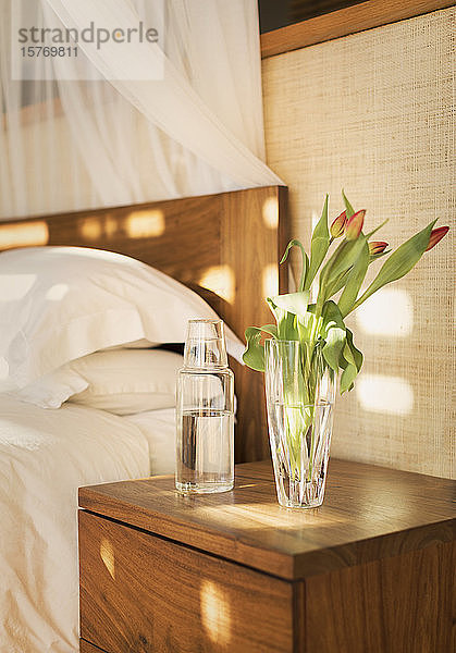 Tulpenstrauß und Wasserkrug auf dem Nachttisch in einem ruhigen Schlafzimmer