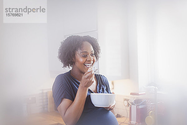 Glückliche schwangere Frau beim Essen in der Küche