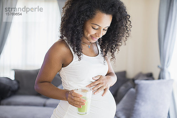 Glückliche junge schwangere Frau trinkt grünen Smoothie