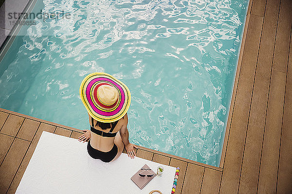 Frau in Sonnenhut und Bikini entspannt am Pool