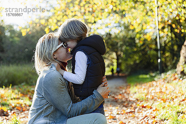 Zärtliche Mutter und Sohn umarmen sich im sonnigen Herbstpark