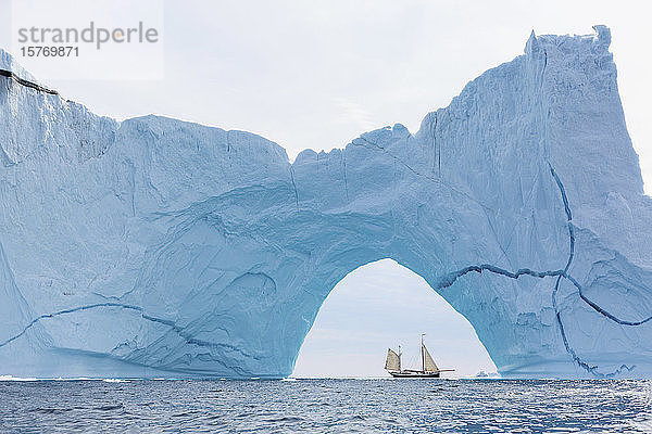 Ein Schiff fährt hinter einer majestätischen Eisbergformation auf dem Atlantik in Grönland