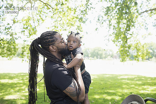 Vater mit langen Zöpfen küsst sein Kleinkind im Park